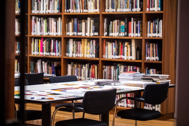 A table, four chairs, and a bookshelf at a library.